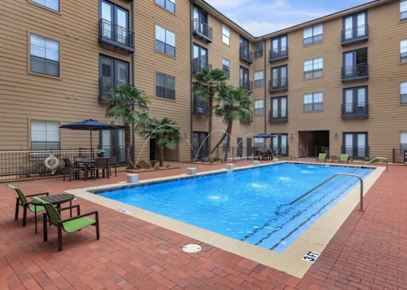 A large swimming pool in front of a brick building with a patio area.
