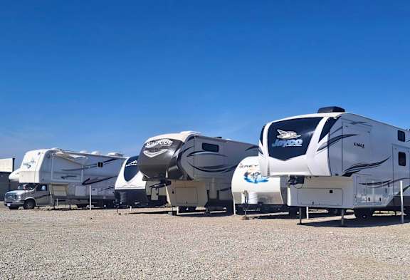 A row of RVs are parked in a lot.