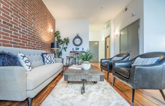 A living room with a grey couch, a coffee table, and a brick wall.