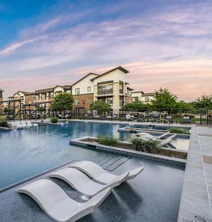a swimming pool with chairs and buildings in the background
