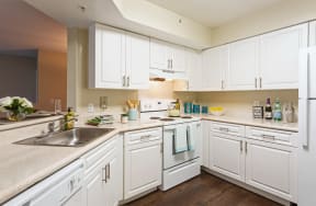 White wood cabinetry with stainless handles , dark wood flooring, with white appliances