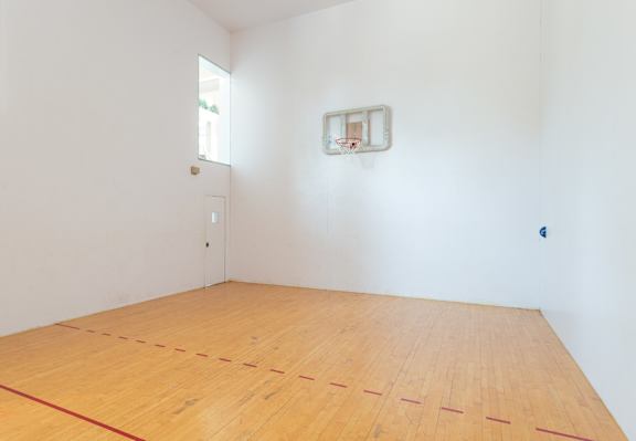 A basketball hoop is mounted on a wall in a room with a wooden floor.