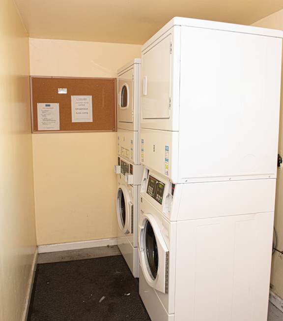 A row of white front loading washing machines are lined up in a laundromat.