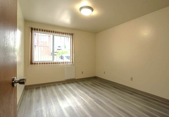 A room with a wooden floor and a window with blinds.