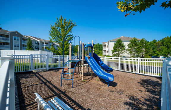 a playground with a blue slide in front of a white fence
