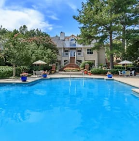 A swimming pool surrounded by trees and chairs.