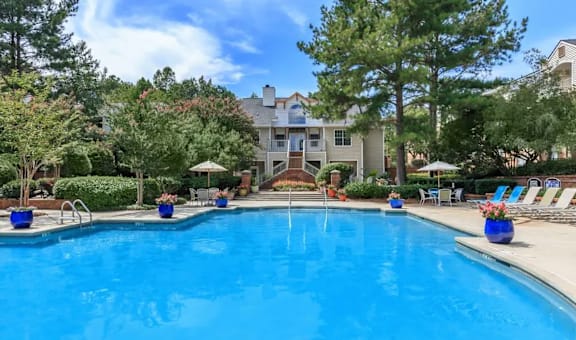A swimming pool surrounded by trees and chairs.