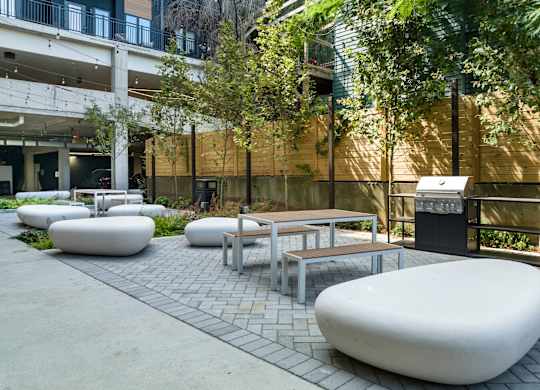 2 BR Apartments In Nulu, KY - Martin On Main - Courtyard With A Grill Surrounded By Greenery With Tables, Chairs, And Large Rocks For Seating