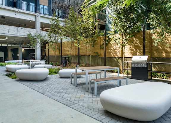 2 BR Apartments In Nulu, KY - Martin On Main - Courtyard With A Grill Surrounded By Greenery With Tables, Chairs, And Large Rocks For Seating