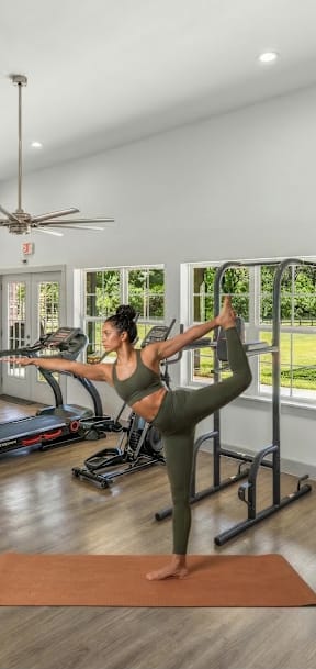 A woman is practicing yoga in a room with a treadmill and exercise bike in the background.