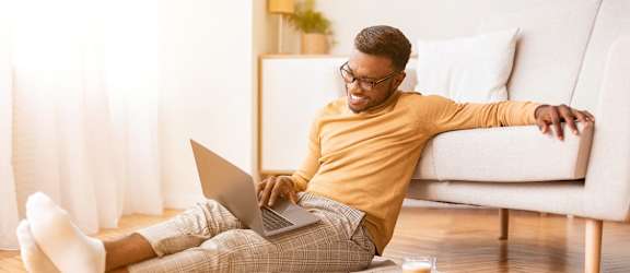 A man is sitting on the floor with his feet up, using a laptop.