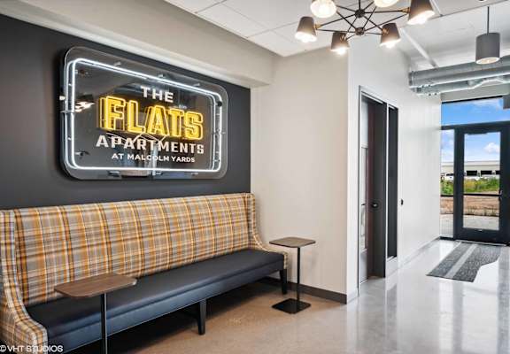 a lounge area with a couch and stool in front of a sign that says the flats apartments