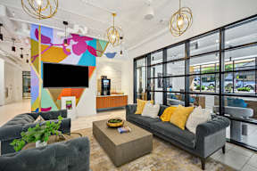 A modern living room with a grey couch, a coffee table, and a colorful abstract painting on the wall.