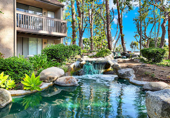 A small waterfall in a garden with a building in the background.