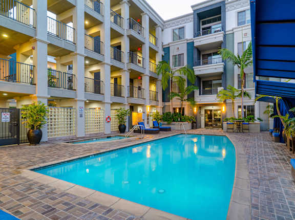 A large swimming pool is surrounded by a patio and apartment buildings at The Adler Apartments, Los Angeles, CA