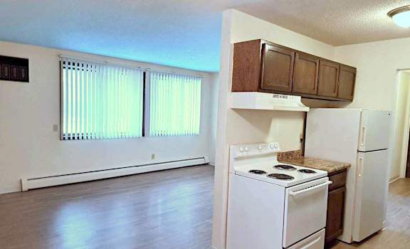 an empty kitchen with white appliances and wood floors