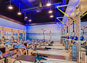 Thumbnail 1 of 7 - A gym with pilates reformers and a blue wall.
