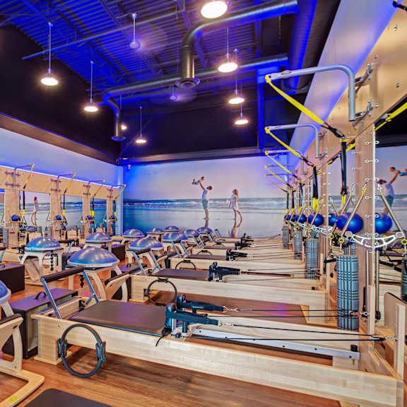 A gym with pilates reformers and a blue wall.