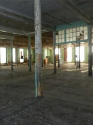 Interior of an old mill showing a large empty space with structural columns, before construction or renovation.