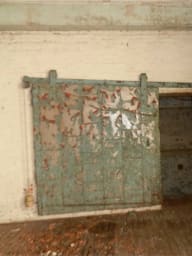 Weathered metal door in Converse Mill Lofts before conversion, set in a dilapidated brick wall.
