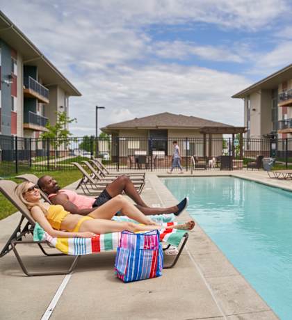 A woman in a yellow bikini lounges by a pool with a man in a pink shirt at Meadowlark Place Apartments, Iowa, 50111