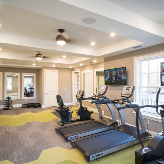 Modern fitness center at Tindall Park Apartments featuring treadmills, an exercise bike, free weights, and mounted TVs.