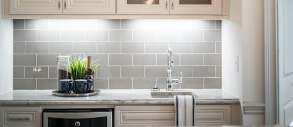 A modern kitchen with cream cabinets, a gray subway tile backsplash, and a small beverage station.