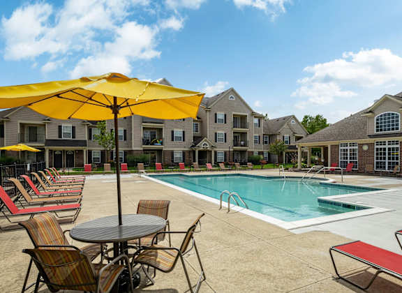 A pool area with chairs and umbrellas in front of apartment buildings.