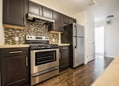 Thumbnail 3 of 11 - Kitchen with stainless steel appliances, hardwood floors, dark wooden cabinets, off white counter tops, and black and white tile patterned back splash