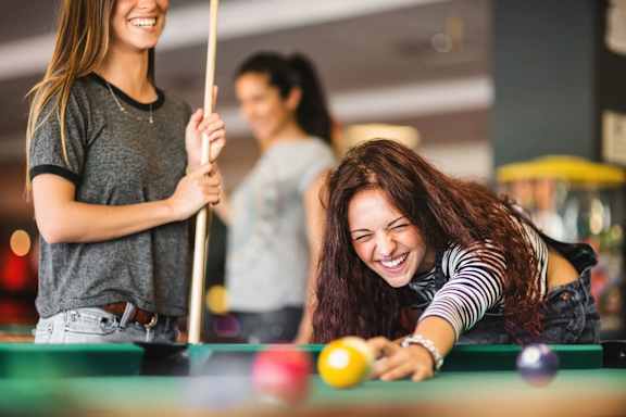 Two women playing pool with a ball on the table.