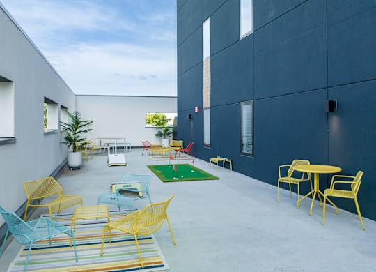 a patio with yellow and blue chairs and tables and a green rug
