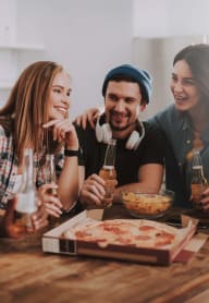 a group of friends sitting around a table drinking beer and eating pizza