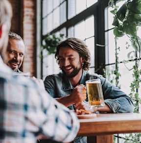 Three men are sitting at a table, laughing and enjoying a beer together.