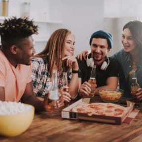 a group of friends sitting around a table drinking beer and eating pizza