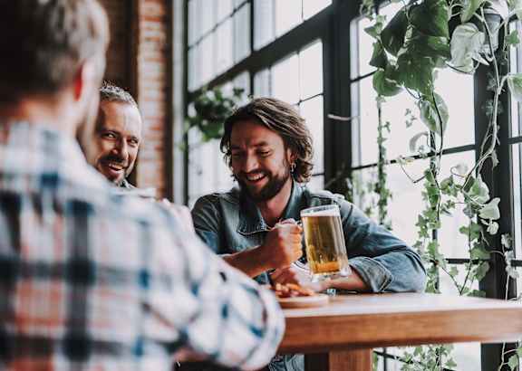 Three men are sitting at a table, laughing and enjoying a beer together.