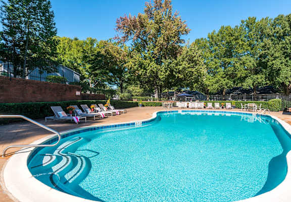 a swimming pool with lounge chairs and trees in the background