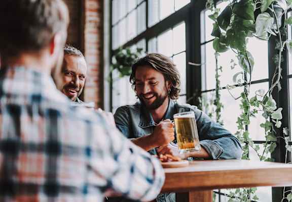 Three men are sitting at a table, laughing and enjoying a beer together.