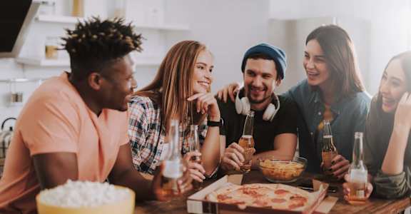 a group of friends sitting around a table drinking beer and eating pizza