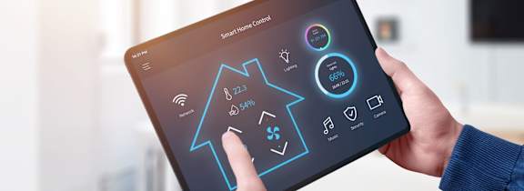 A person is holding a tablet with a smart home interface on the screen.