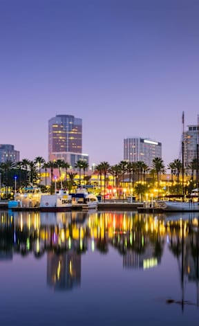 A city skyline is reflected in the water at dusk.