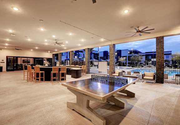 a large patio with a ping pong table and a pool in the background and cocktail bar