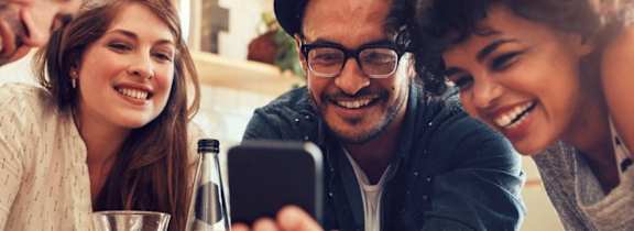A group of people are gathered around a smartphone, seemingly engaged in a lively conversation.