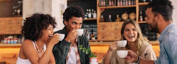 Four people are having a conversation over coffee in a cozy café setting.