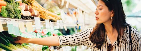 A woman is shopping for vegetables in a grocery store.