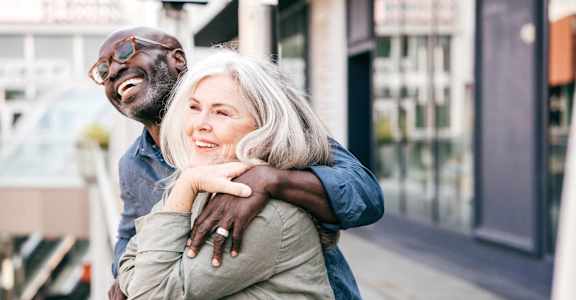 an older man and woman hugging on a city street