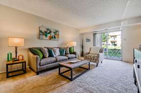 A cozy living room with plush carpet flooring and natural light from sliding glass doors to a private patio.