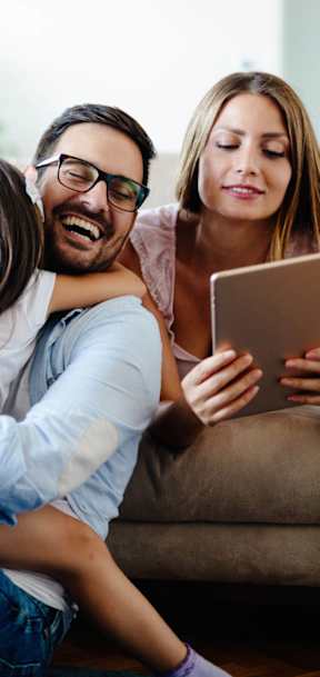 A family of three is sitting on a couch with a tablet in hand.