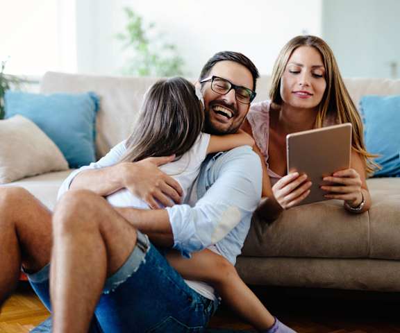 A family of three is sitting on a couch with a tablet in hand.