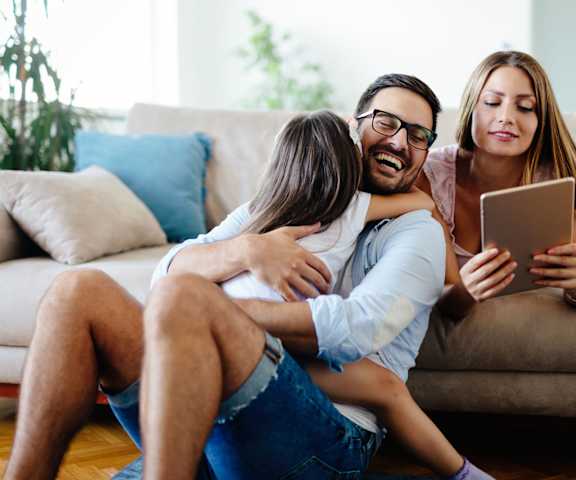 A man is sitting on the floor with a woman and a child, all looking at a tablet.