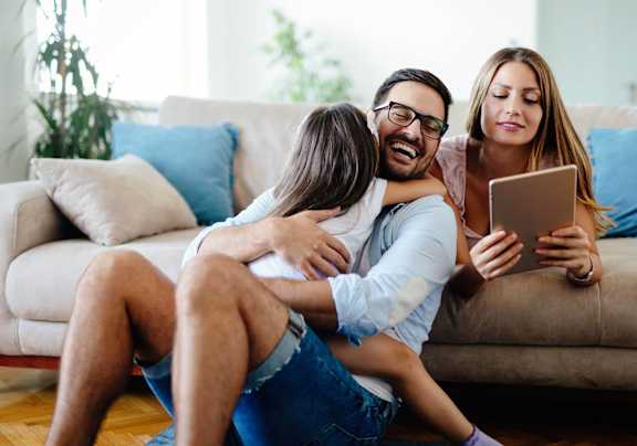 A man is sitting on the floor with a woman and a child, all looking at a tablet.
